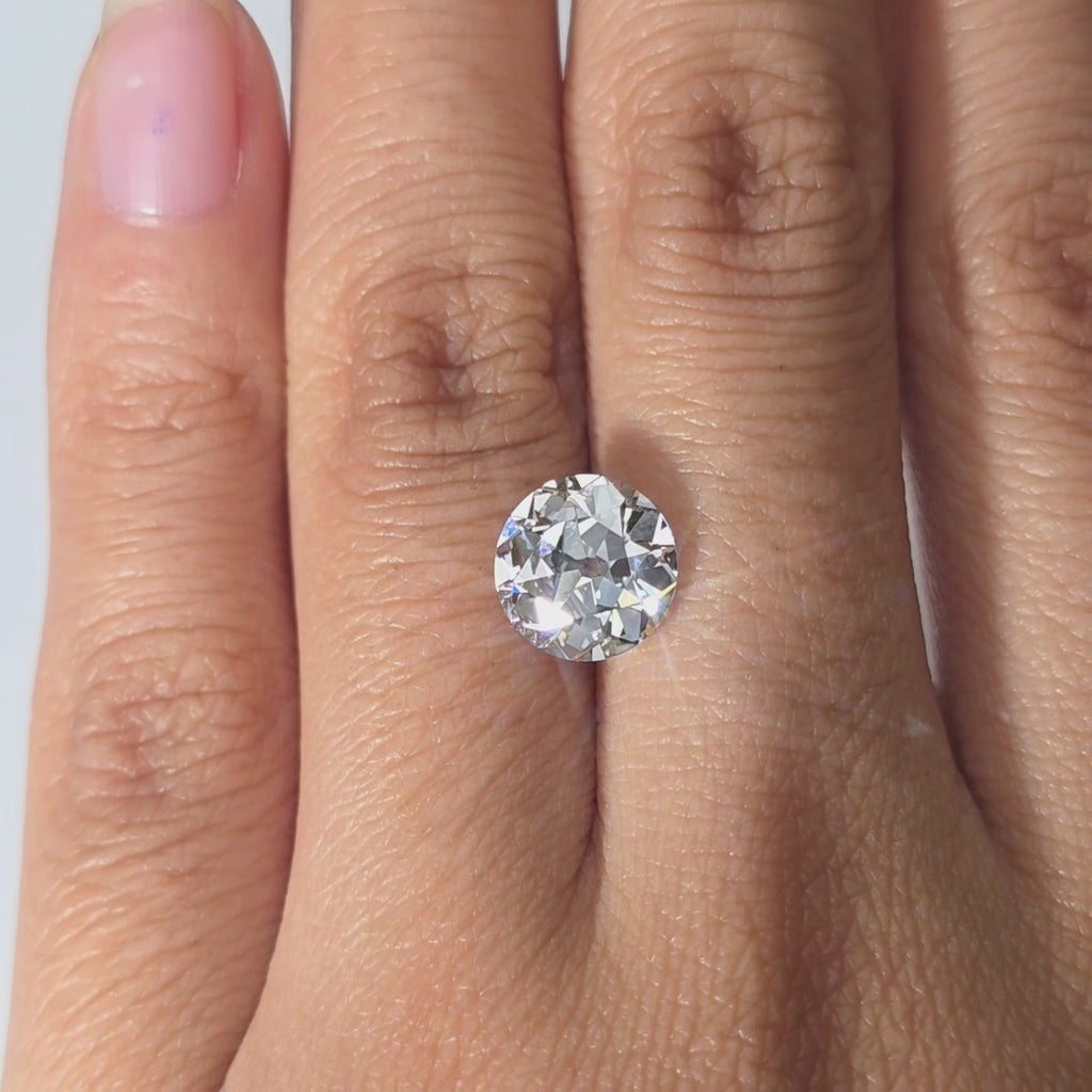 A hand presents a 2.51ct round European cut lab diamond in warm indoor light.