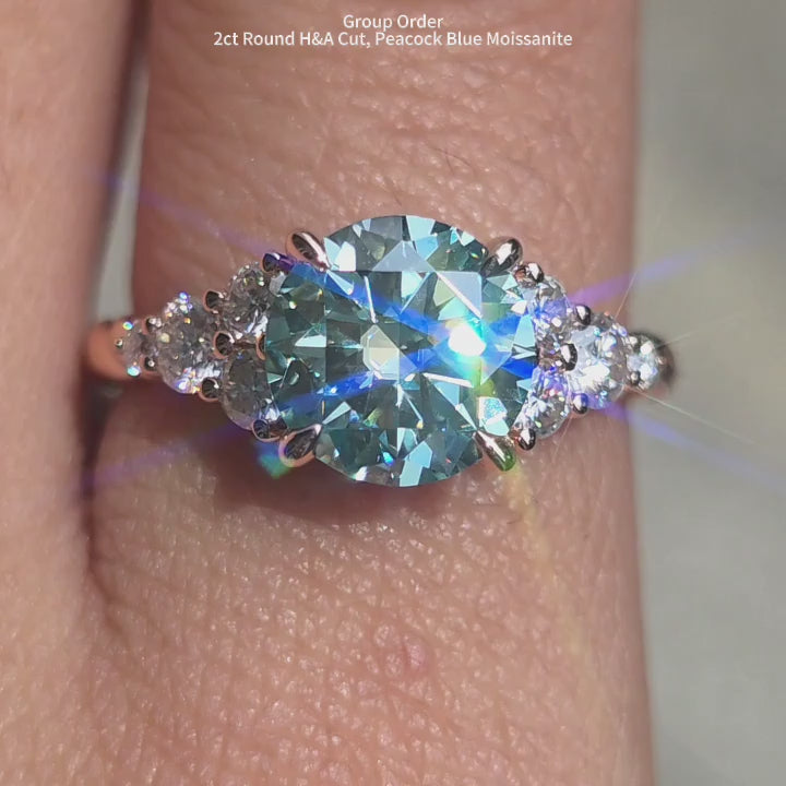 DovEggs round side stones twisted shank peacock blue moissanite engagement ring