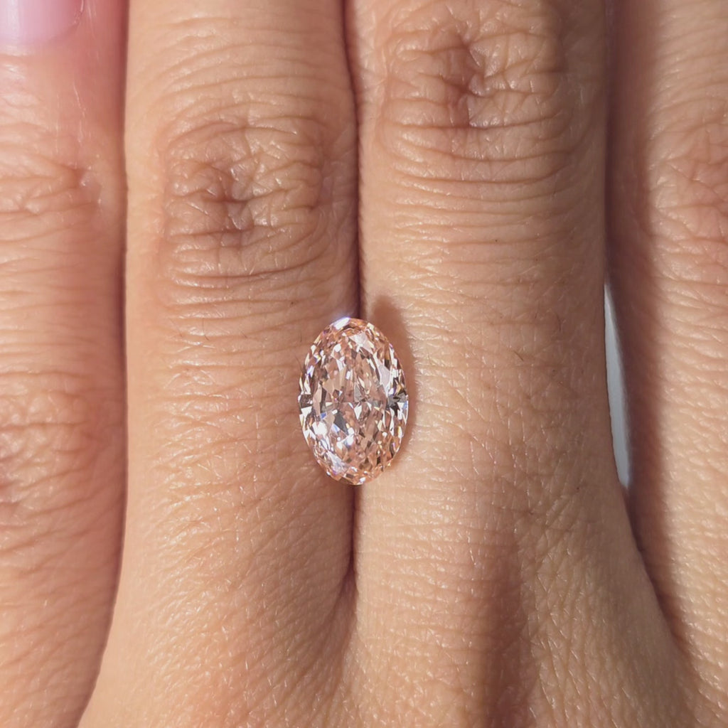 Hand modeling a 2.07ct oval cut fancy vivid pink VVS1 lab diamond in warm indoor light.