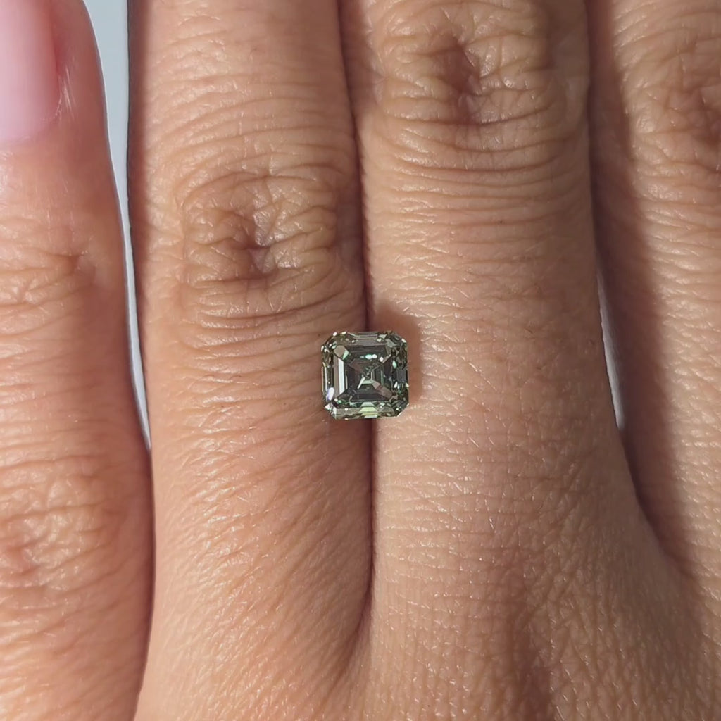 Hand presenting a 1.03ct asscher cut fancy vivid green VVS1 lab diamond in warm indoor light.