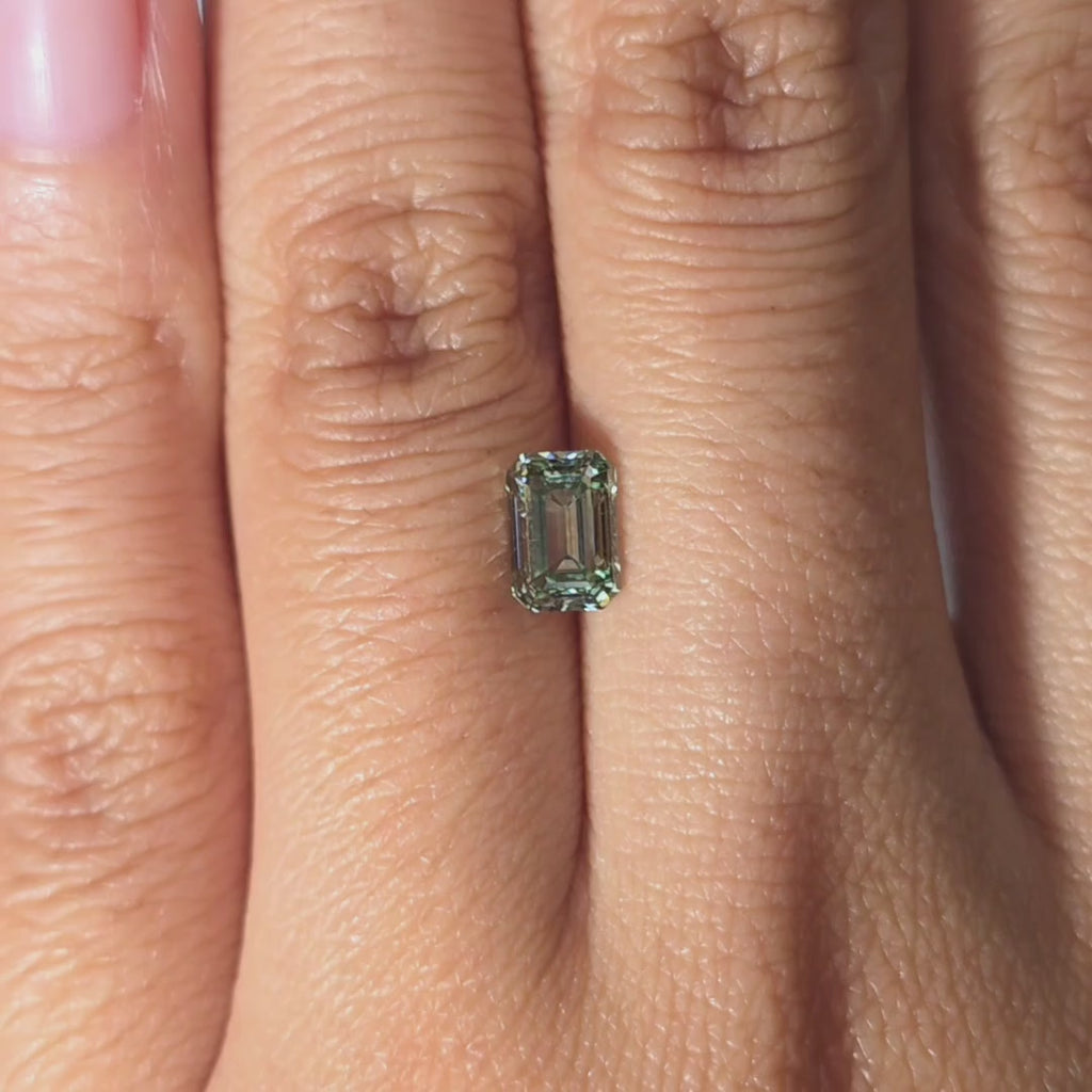 Hand showcasing a 1.08ct emerald cut fancy vivid green VVS1 lab diamond in warm indoor light.