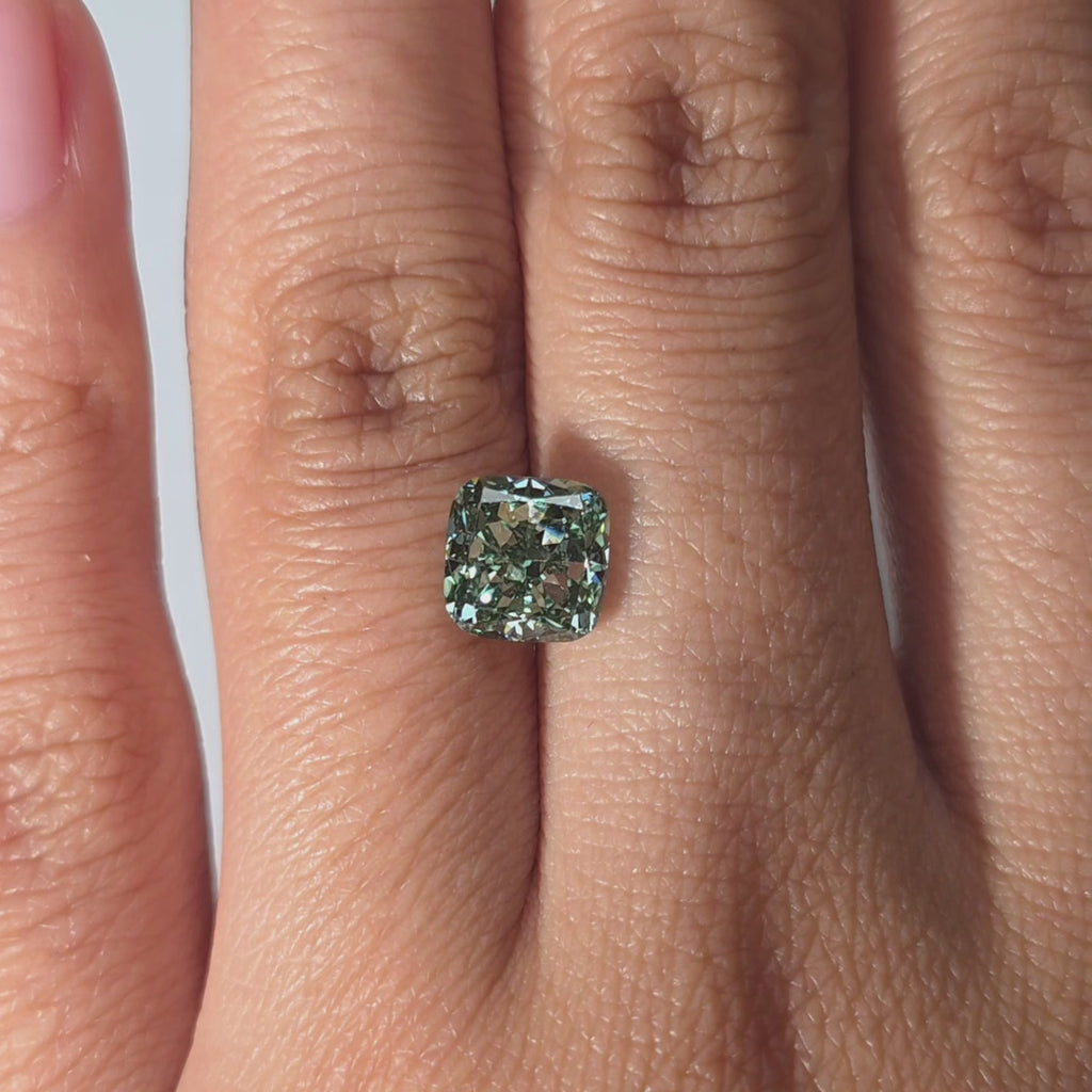 Hand showcasing a 2.07ct cushion cut fancy vivid green lab diamond in warm indoor lighting.
