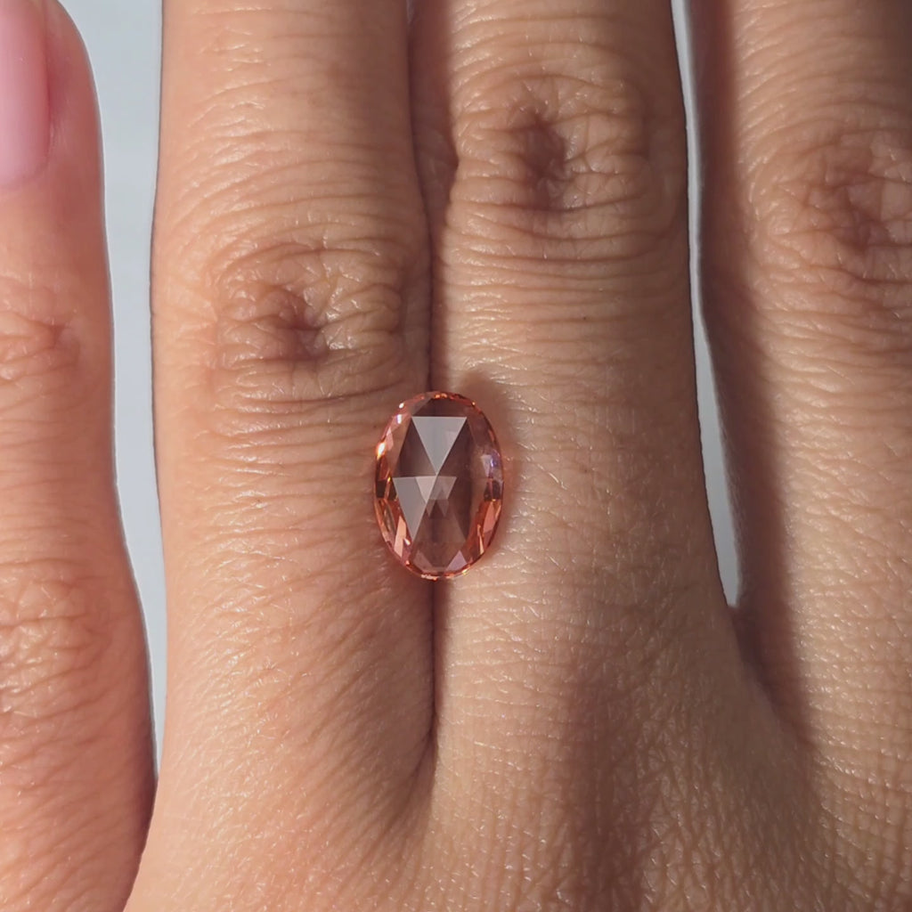 Hand showcasing a 1.75ct oval rose cut fancy vivid pink VVS1 lab diamond in warm indoor light.