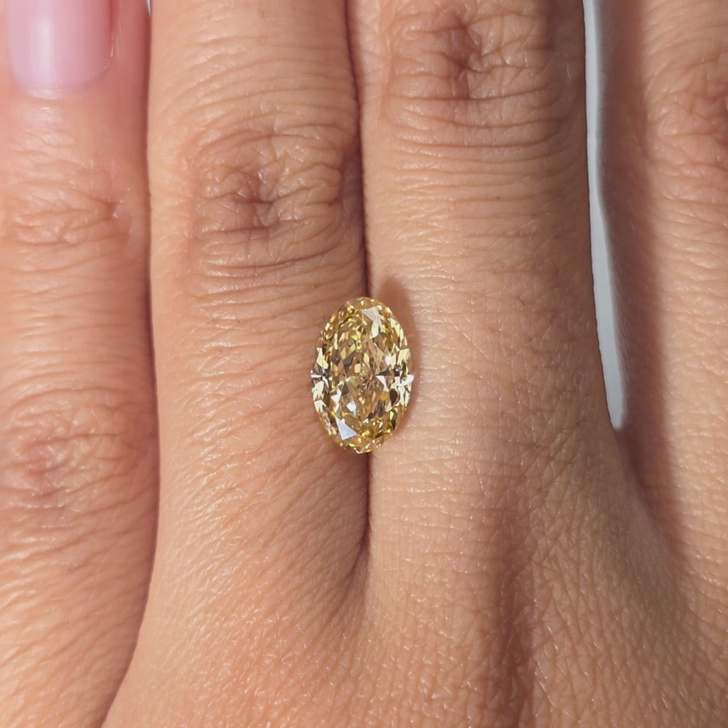 Hand showcasing a 2.22ct oval cut fancy vivid yellow VVS1 lab diamond in warm indoor light.