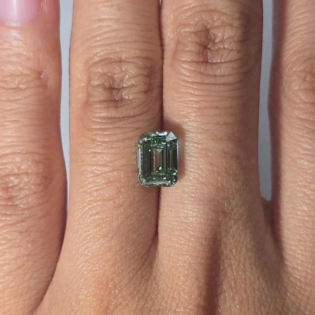 Hand presenting a 2.54ct emerald cut fancy vivid green VS1 lab diamond in warm indoor light.