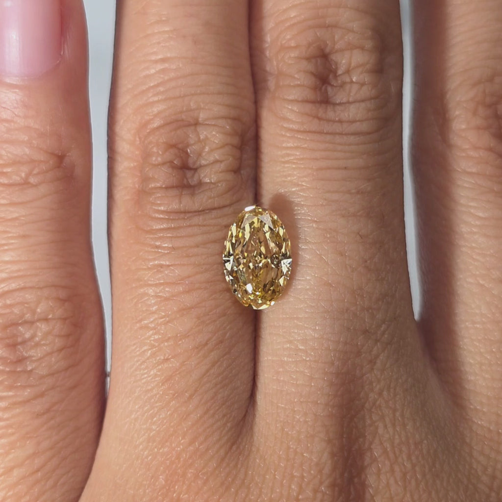 A hand showcases a 2.09ct oval cut fancy vivid yellow lab diamond in warm light.