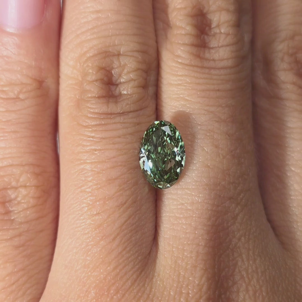 Hand showcasing a 2.24ct oval cut fancy vivid green VVS1 lab diamond in warm indoor light.