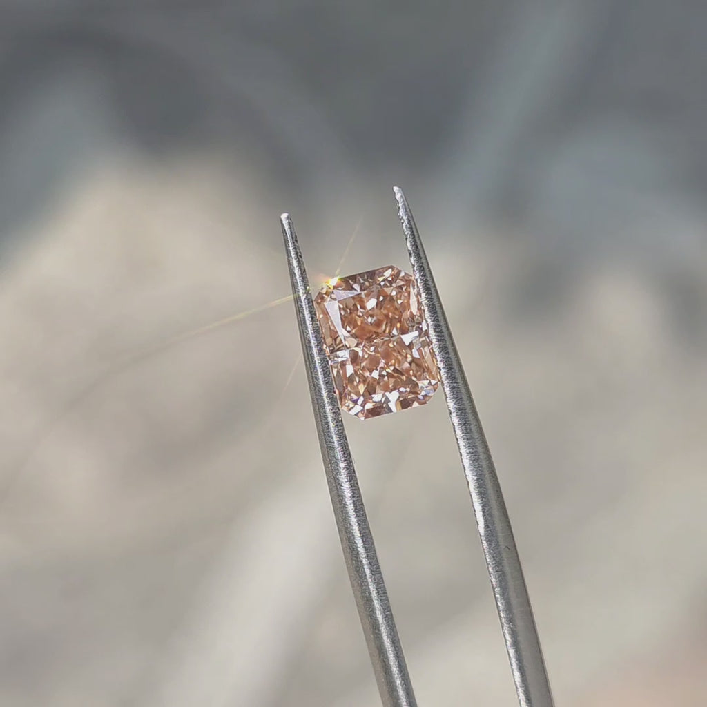 A 2.08ct radiant brilliant cut fancy vivid pink lab diamond sparkles in outdoor sunlight.