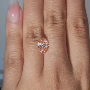 Close-up of 2.10ct Oval fancy vivid pink diamond in warm handheld lighting