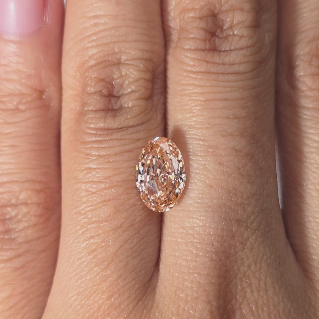 Hand showcasing a 2.20ct oval cut fancy vivid pink lab diamond in warm indoor light.