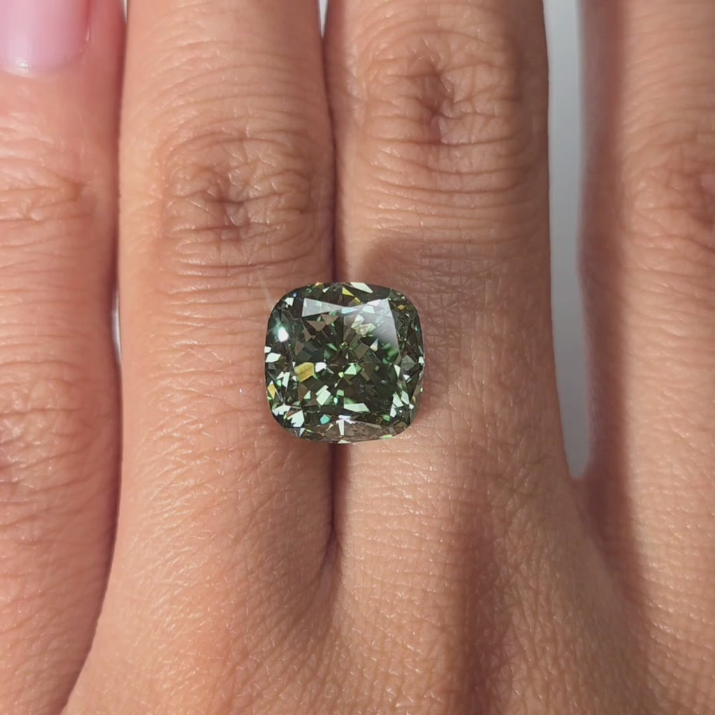 Hand modeling a 6.68ct cushion cut fancy vivid green lab diamond in warm indoor light.