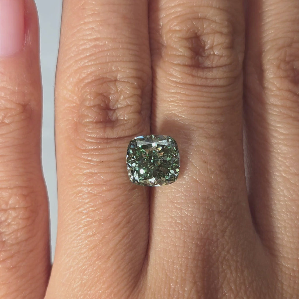 A 2.76ct cushion cut fancy vivid green lab diamond held in hand under warm light.