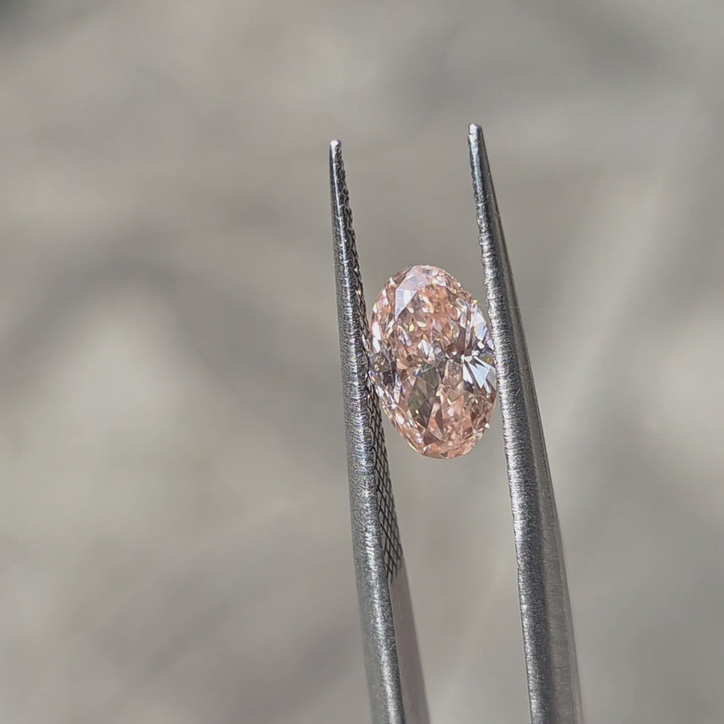 1.05ct oval brilliant cut fancy light pink VVS2 lab diamond showing delicate pink hue in outdoor sunlight.