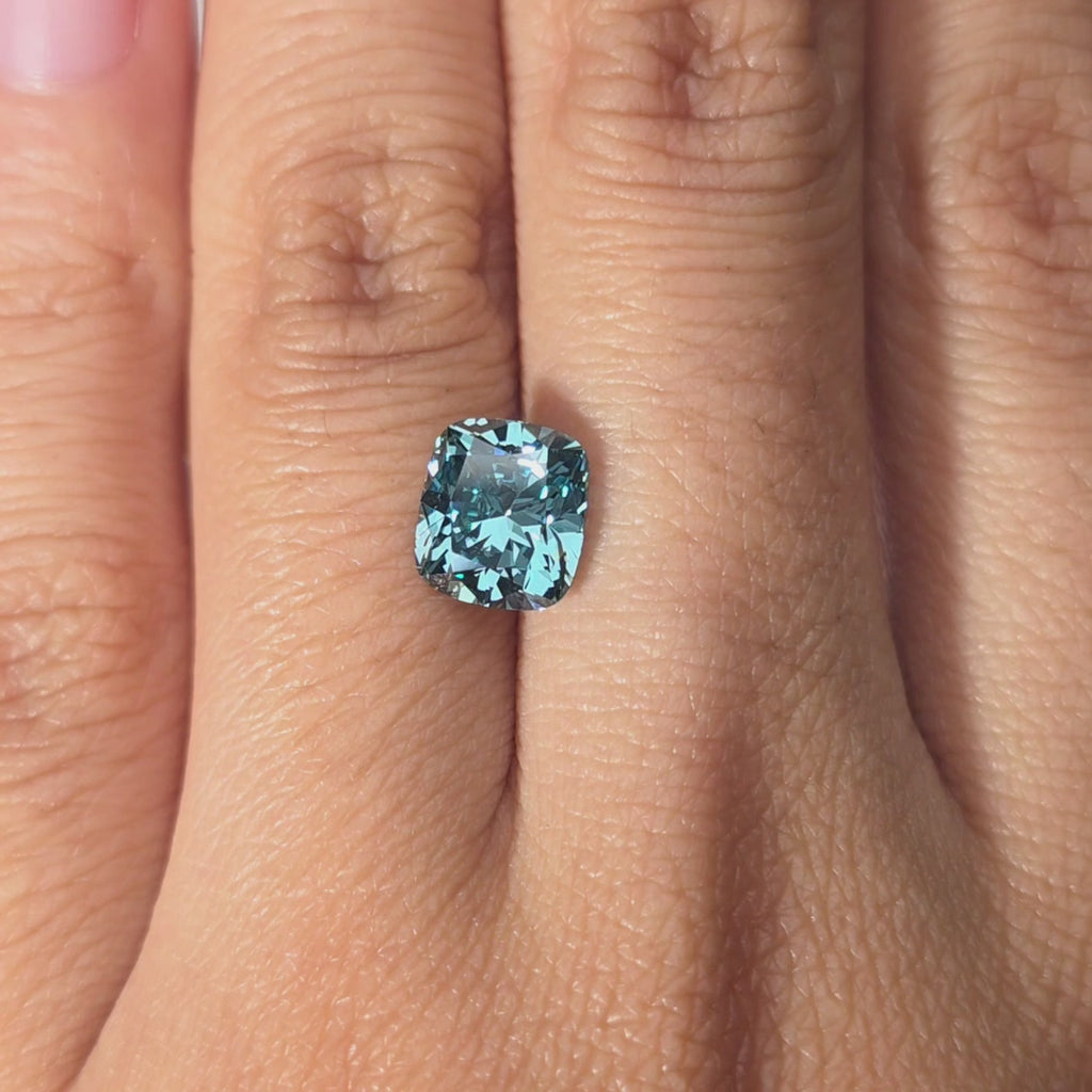 Hand modeling a 2.14ct cushion cut fancy vivid blue lab diamond in warm indoor setting.