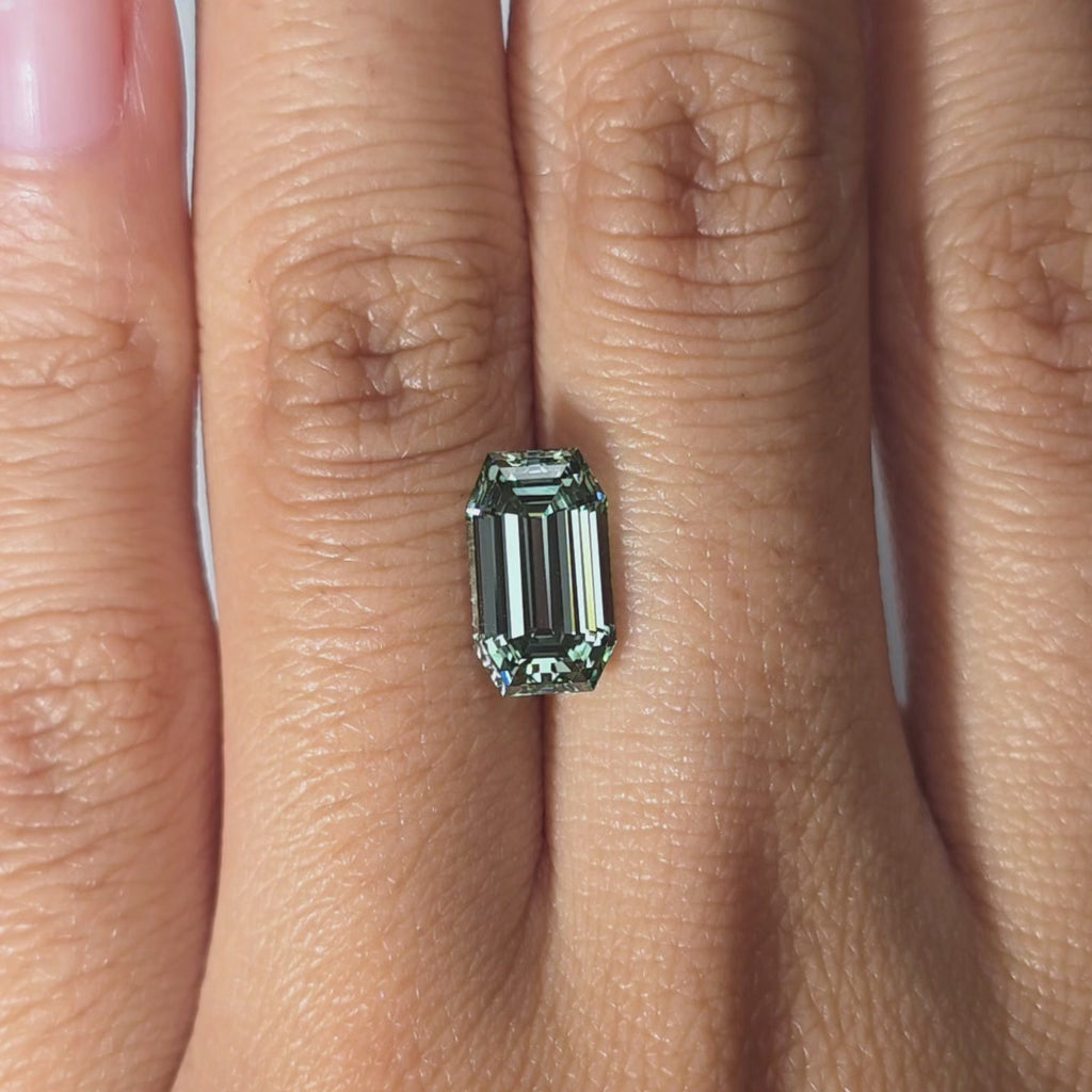 Hand modeling a 2.85ct old emerald cut fancy vivid green VVS1 lab diamond in warm indoor light.