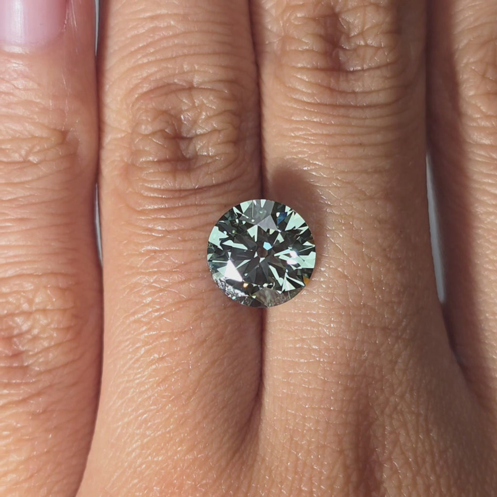 Hand presenting a 3.23ct round old European cut fancy vivid green VVS1 lab diamond in warm indoor light.