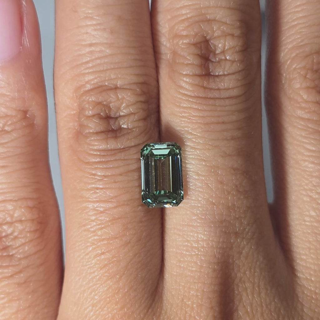 Hand modeling a 2.52ct emerald cut fancy vivid green VVS1 lab diamond in warm indoor light.