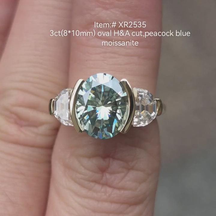 3ct oval H&A cut Peacock Blue moissanite engagement ring with half-moon diamond side stones in two-tone gold tension setting, shown on hand in natural light 