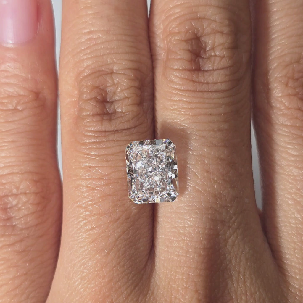 A hand modeling a 3.65ct radiant cut lab diamond indoors under warm light.