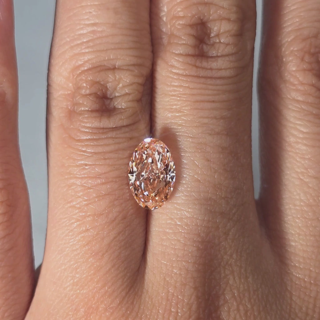 Hand modeling a 2.29ct oval cut fancy vivid pink VS1 lab diamond in warm indoor light.