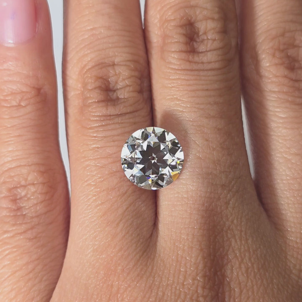 Hand modeling a 4.02ct round European cut lab diamond in warm indoor setting.