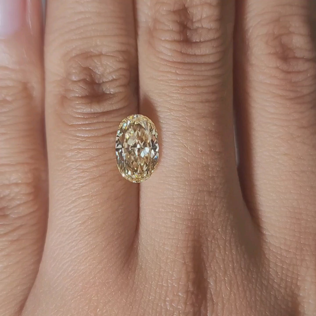 Finger-modeled video of 2.27ct yellow oval diamond under warm lighting