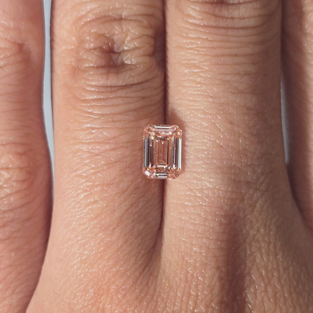 Hand showcasing a 1.05ct emerald cut fancy vivid pink VS1 lab diamond in warm indoor light.