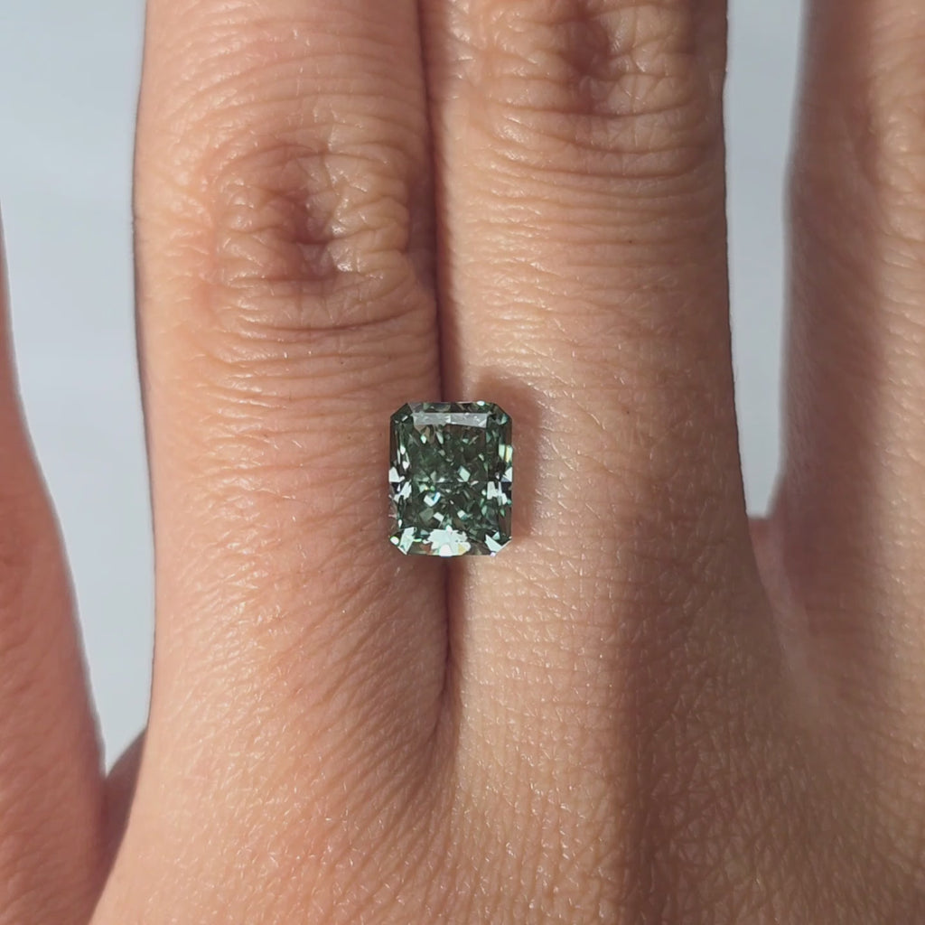 A 1.78ct radiant cut fancy vivid green lab diamond in hand, indoor warm light.