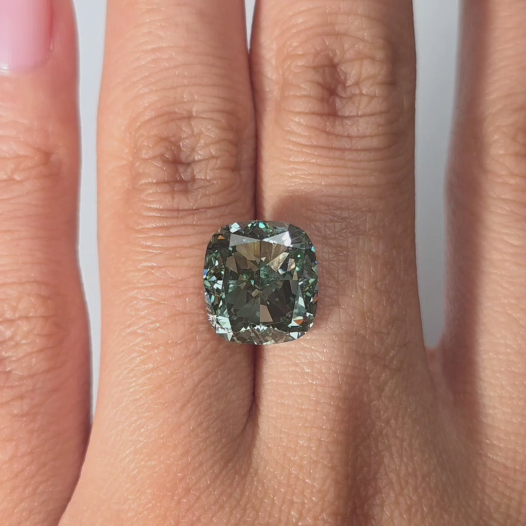 A hand showcases a 7.18ct cushion cut fancy vivid green lab diamond in warm indoor light.