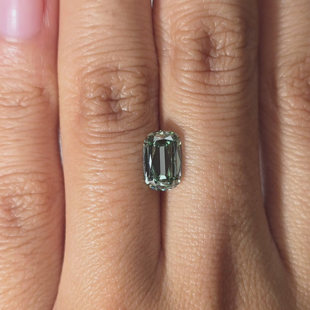 Hand showcasing a 1.88ct cushion old mine cut fancy vivid green VVS1 lab diamond in warm indoor light.