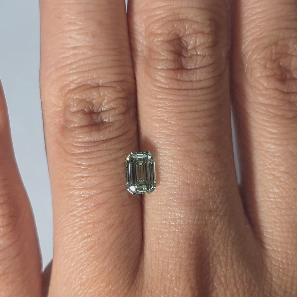 Hand showcasing a 1.10ct emerald cut fancy vivid green VVS1 lab diamond in warm indoor light.