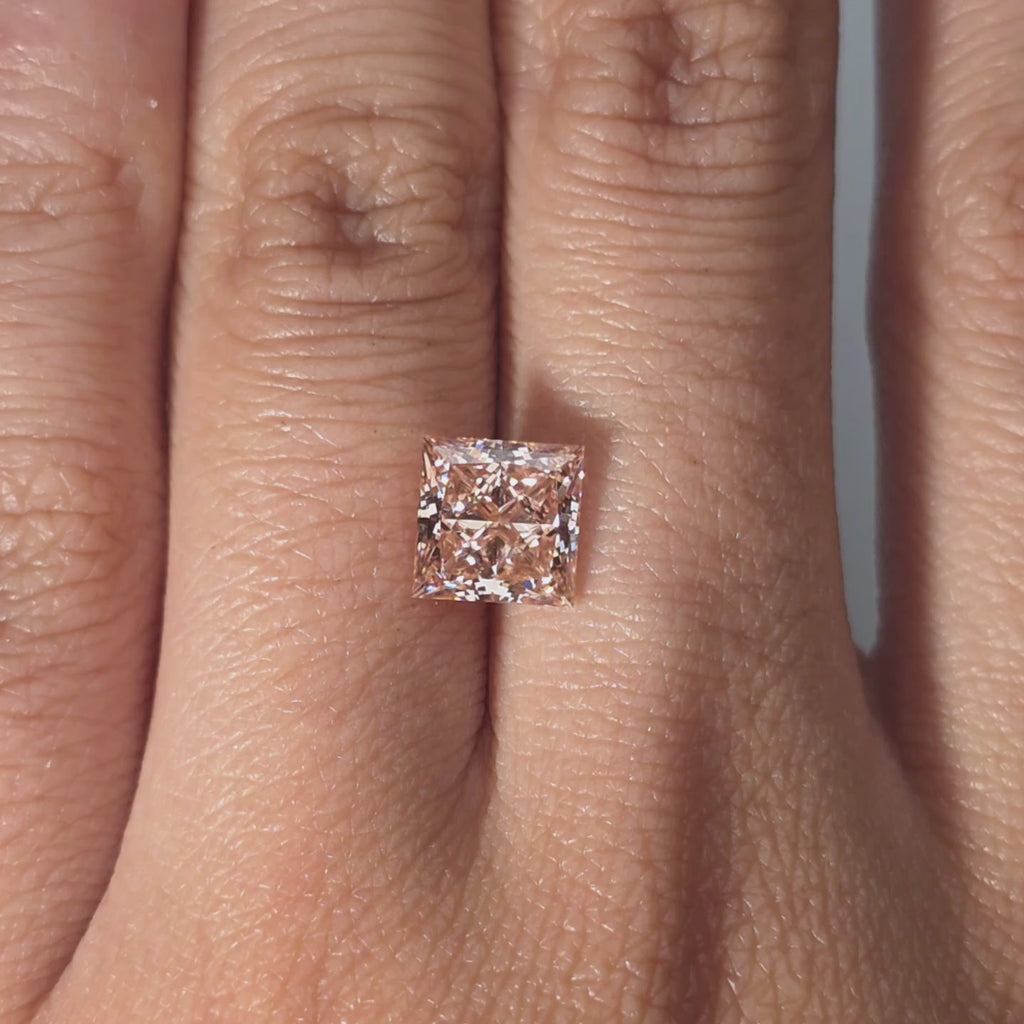 Hand presenting a 2.08ct princess cut fancy vivid pink VS1 lab diamond in warm indoor light.