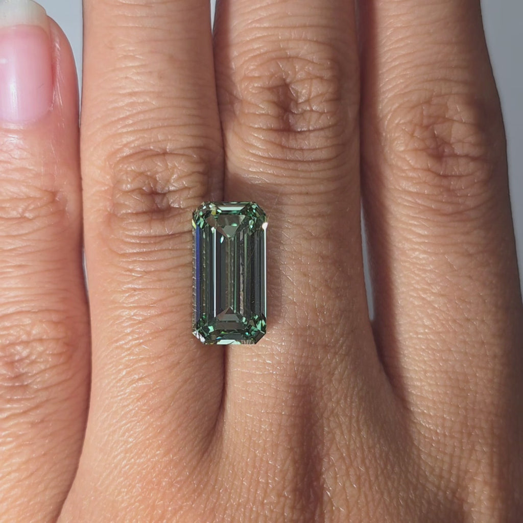 Hand modeling a 6.04ct emerald cut fancy vivid green VVS1 lab diamond in warm indoor light.