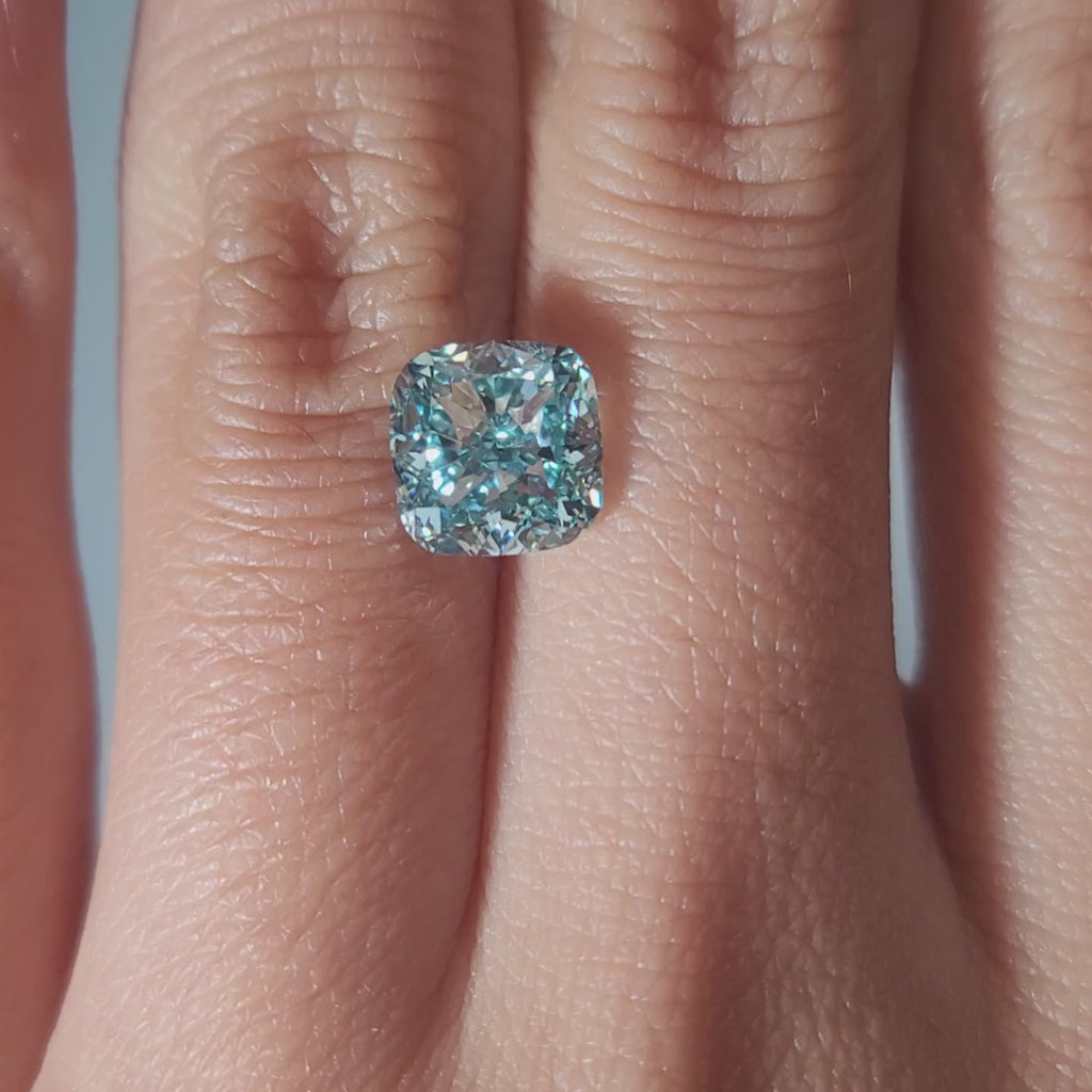 "Hand-modeled video of 2.468ct bluish green cushion diamond in warm indoor lighting"