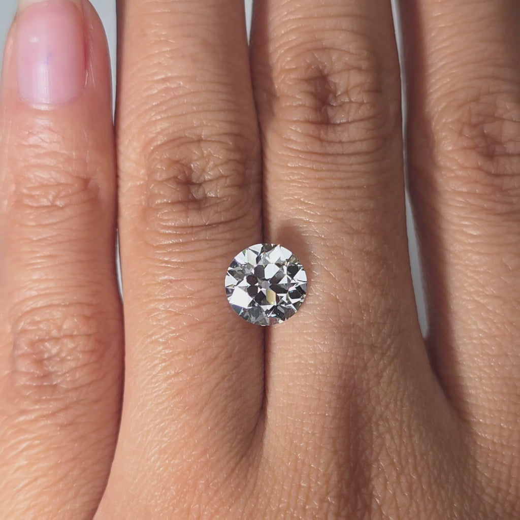 Hand showcasing a 2.10ct round European cut D color VVS1 lab diamond in warm indoor light.