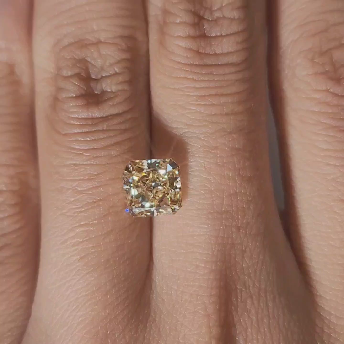 Close-up hand video displaying 2.312ct yellow radiant diamond in cozy indoor light