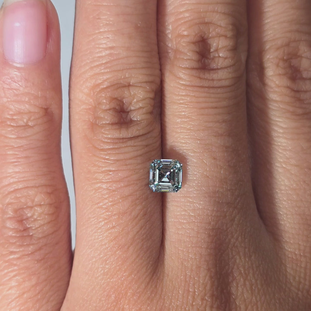 Hand showcasing a 1.00ct asscher cut fancy vivid blue lab diamond in warm light.