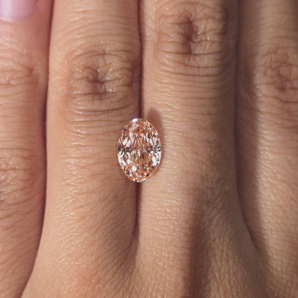 Hand modeling a 2.14ct oval cut fancy vivid pink lab diamond in warm indoor setting.