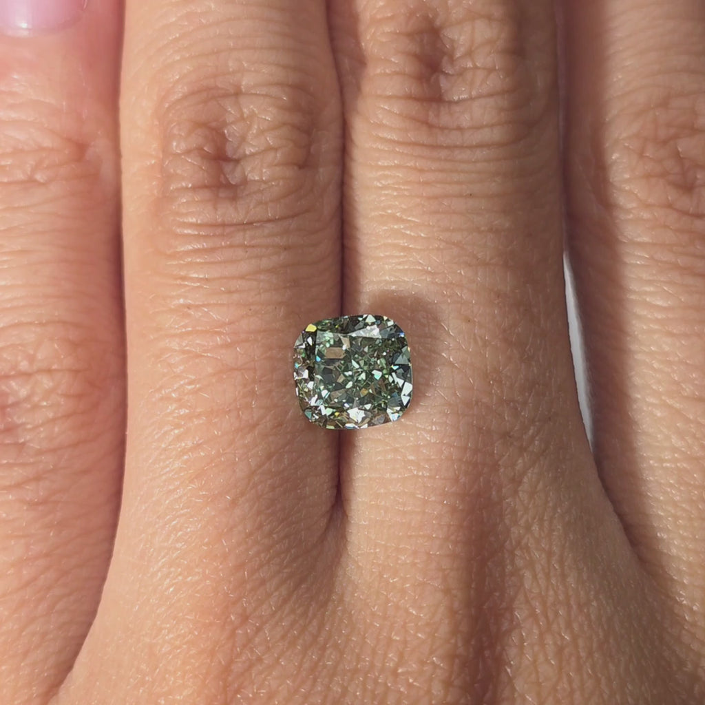 Hand modeling a 2.24ct fancy vivid green cushion brilliant cut lab diamond indoors.