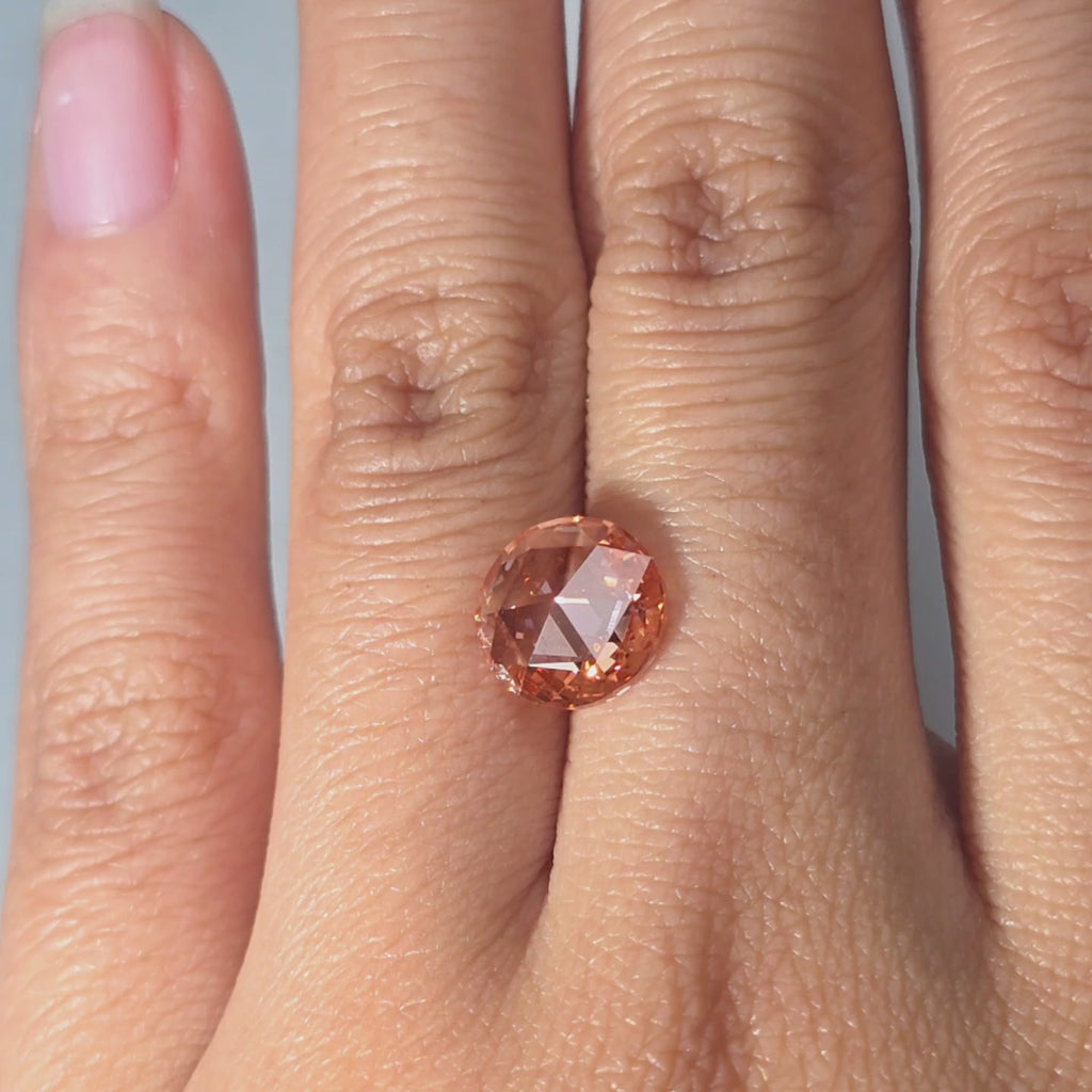 Hand presenting a 2.43ct round rose cut fancy vivid pink VVS2 lab diamond in warm indoor light.