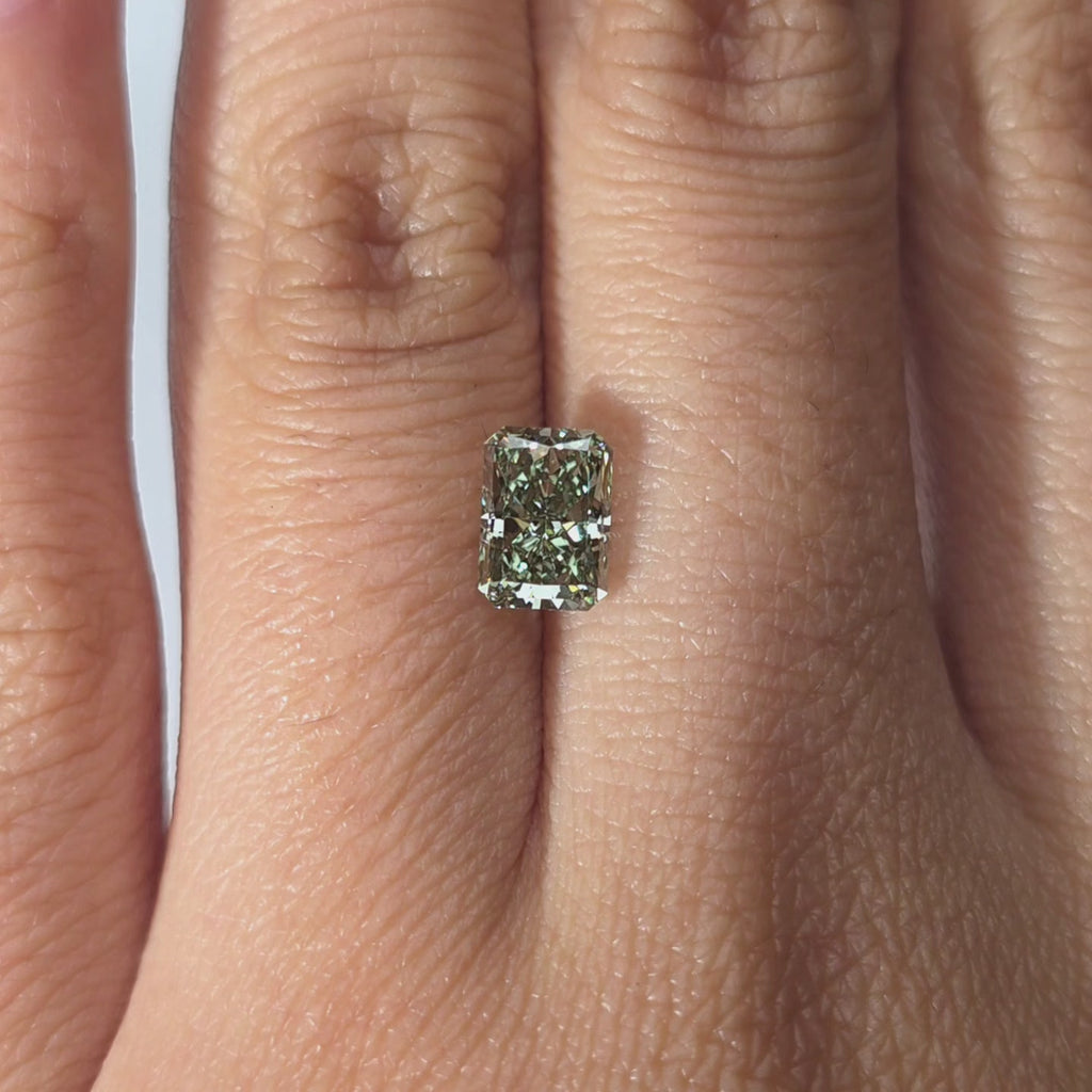 Hand presenting a 1.27ct radiant cut fancy vivid green VVS1 lab diamond in warm indoor light.