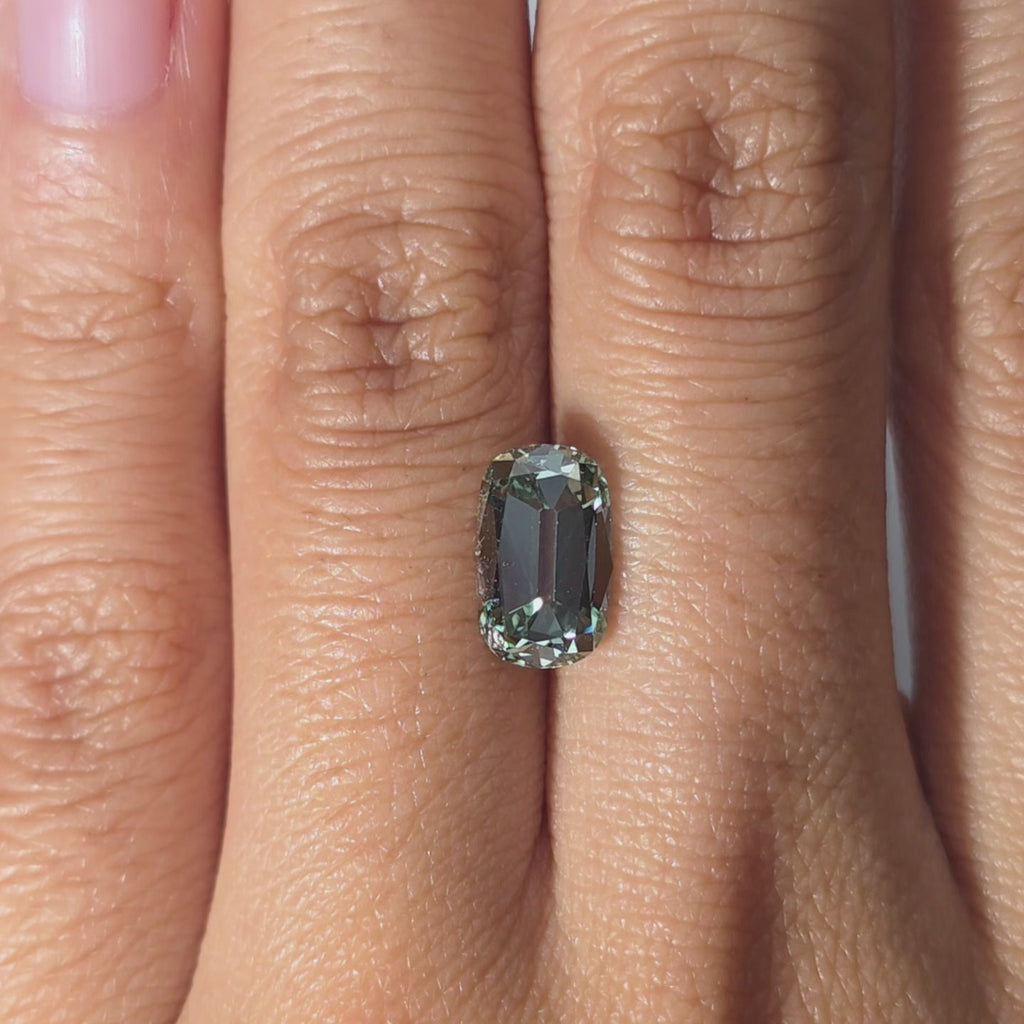 Hand modeling a 2.19ct cushion old mine cut fancy vivid green VS1 lab diamond in warm indoor light.