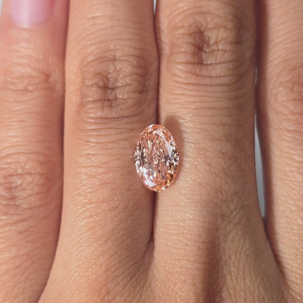 A hand presents a 2.31ct oval cut fancy vivid pink lab diamond under warm light.
