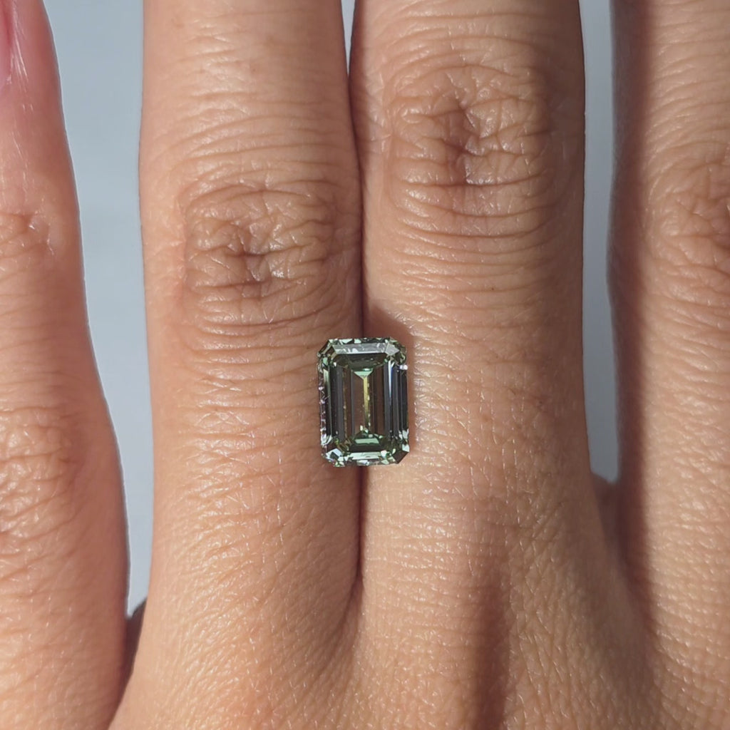 Hand modeling a 2.02ct emerald cut fancy vivid green VVS1 lab diamond in warm indoor light.