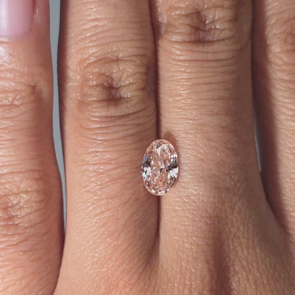 Hand presenting a 1.05ct oval cut fancy light pink VVS2 lab diamond in warm indoor light.