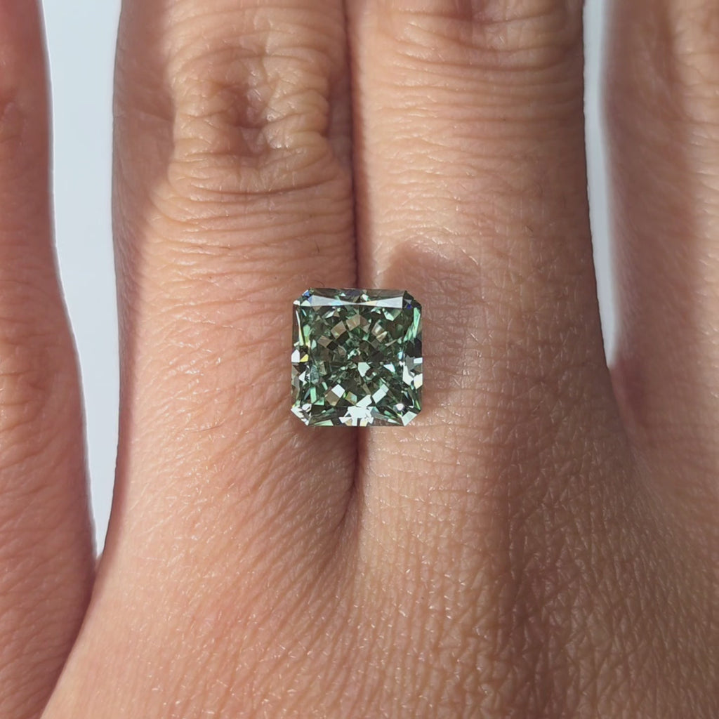 Hand modeling a 3.09ct radiant cut fancy vivid green VVS2 lab diamond in warm indoor light.