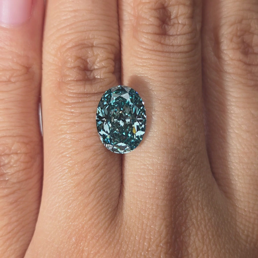 Hand presenting a 4.54ct oval cut fancy vivid blue lab diamond in warm indoor light.