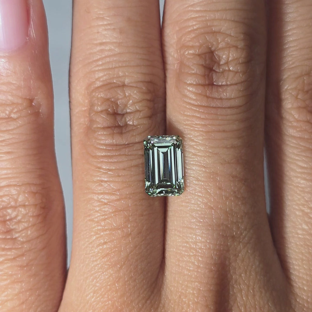 Hand presenting a 2.26ct emerald cut fancy vivid green VVS1 lab diamond in warm indoor light.
