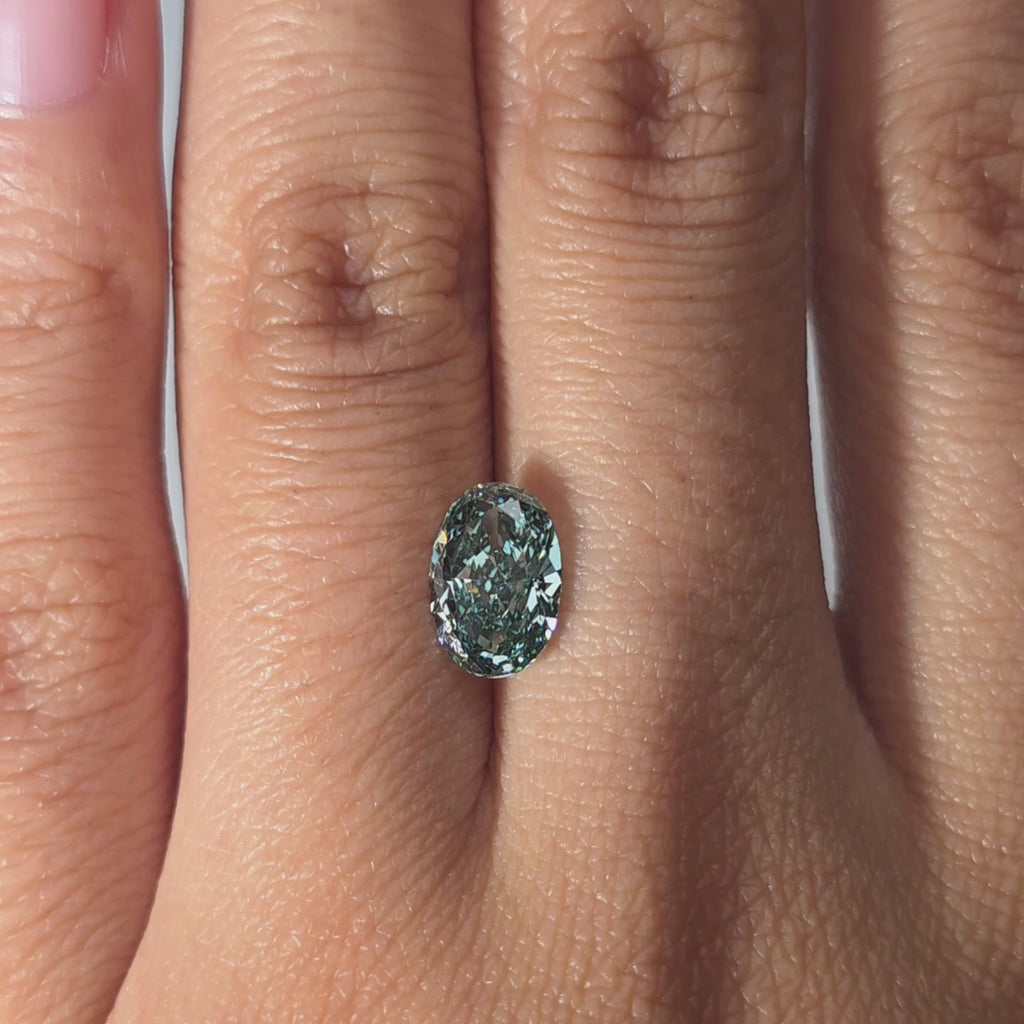 Hand modeling a 1.59ct oval cut fancy vivid green VVS1 lab diamond in warm indoor light.