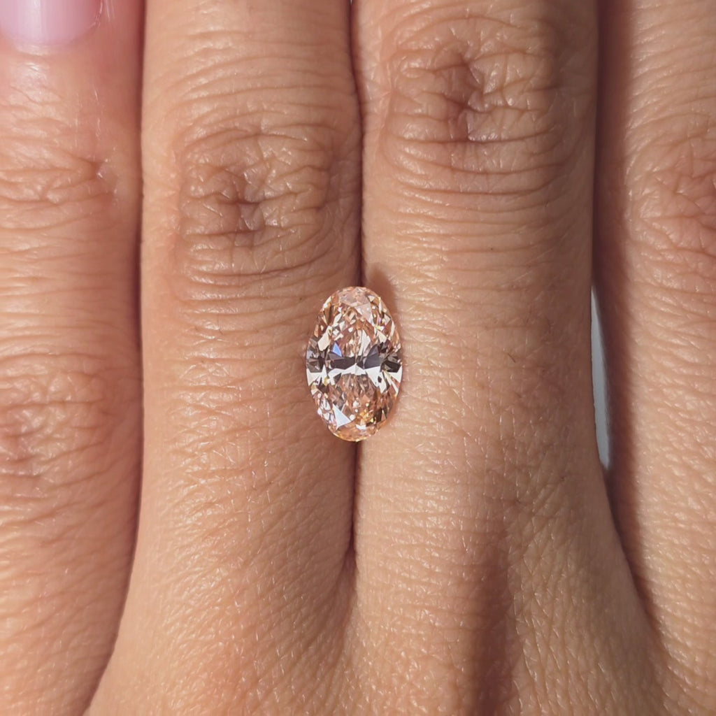 Hand presenting a 1.56ct oval cut fancy vivid pink VVS2 lab diamond in warm indoor light.